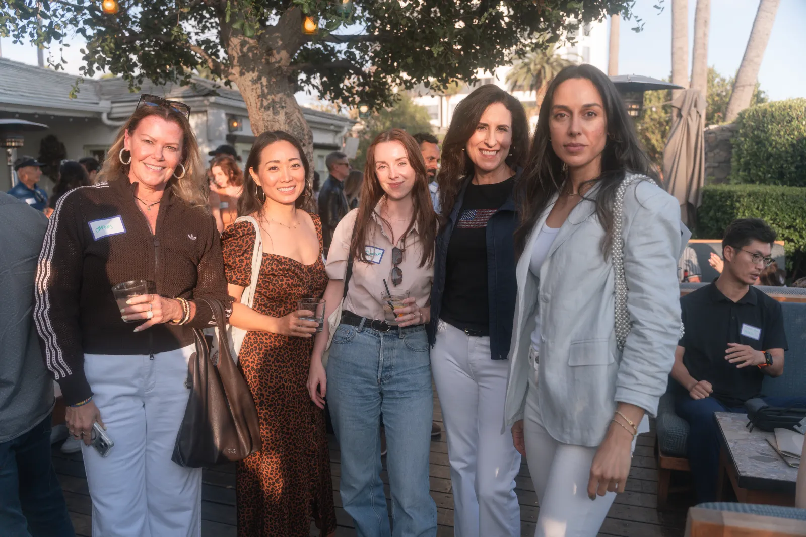 Five attendees gathered for a group photo, drinks in hand, with the crowd and the Bungalow's string lights behind them.