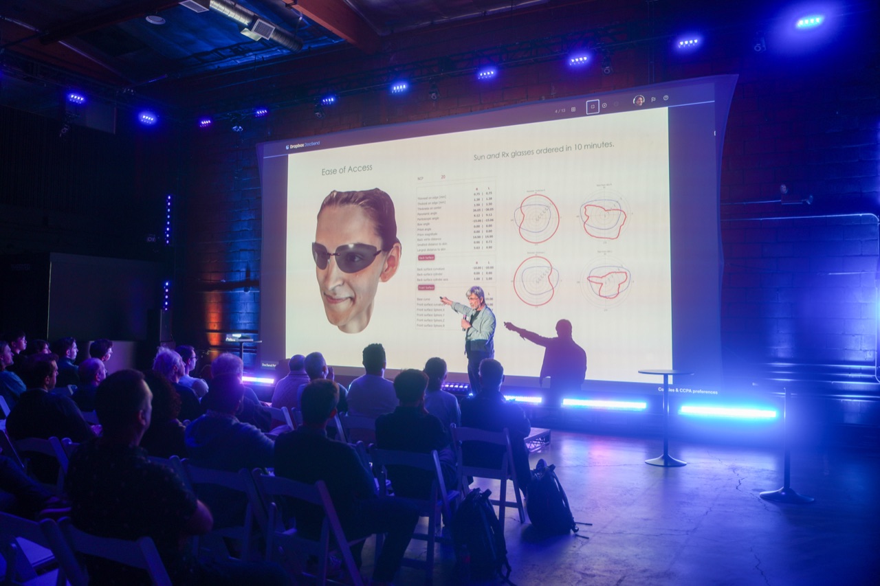 Two speakers on stage gesturing in front of an Ease of Access slide with sunglasses illustration