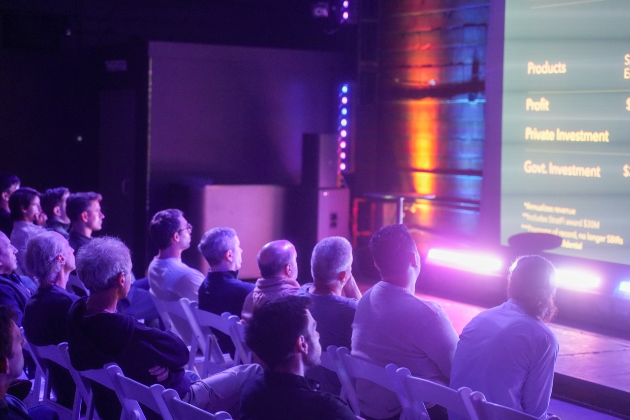 Close shot of Startup Arena attendees packed into rows of chairs, faces lit by stage light as they listen