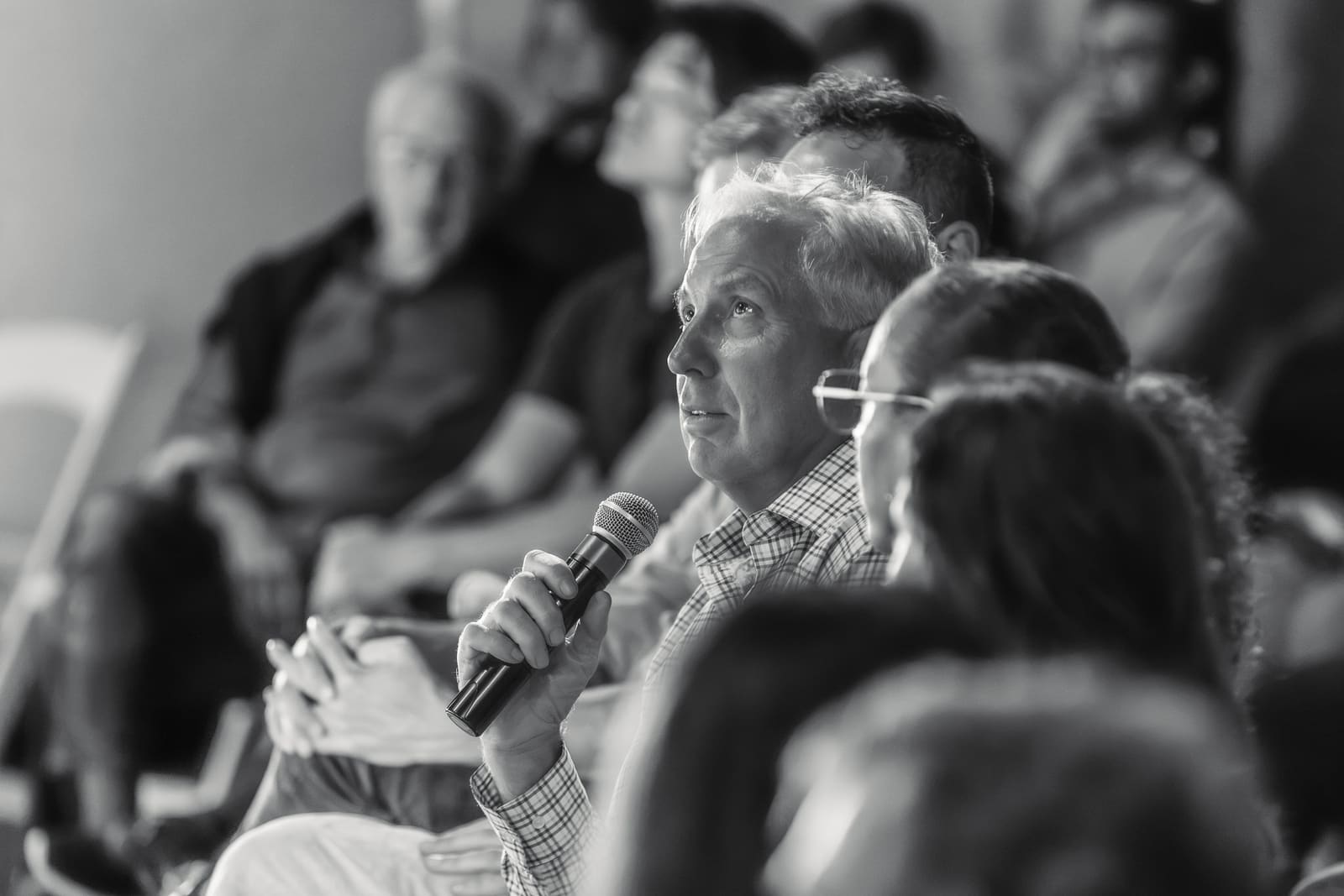 Jim Armstrong seated among the audience, speaking into a handheld mic during Q&A