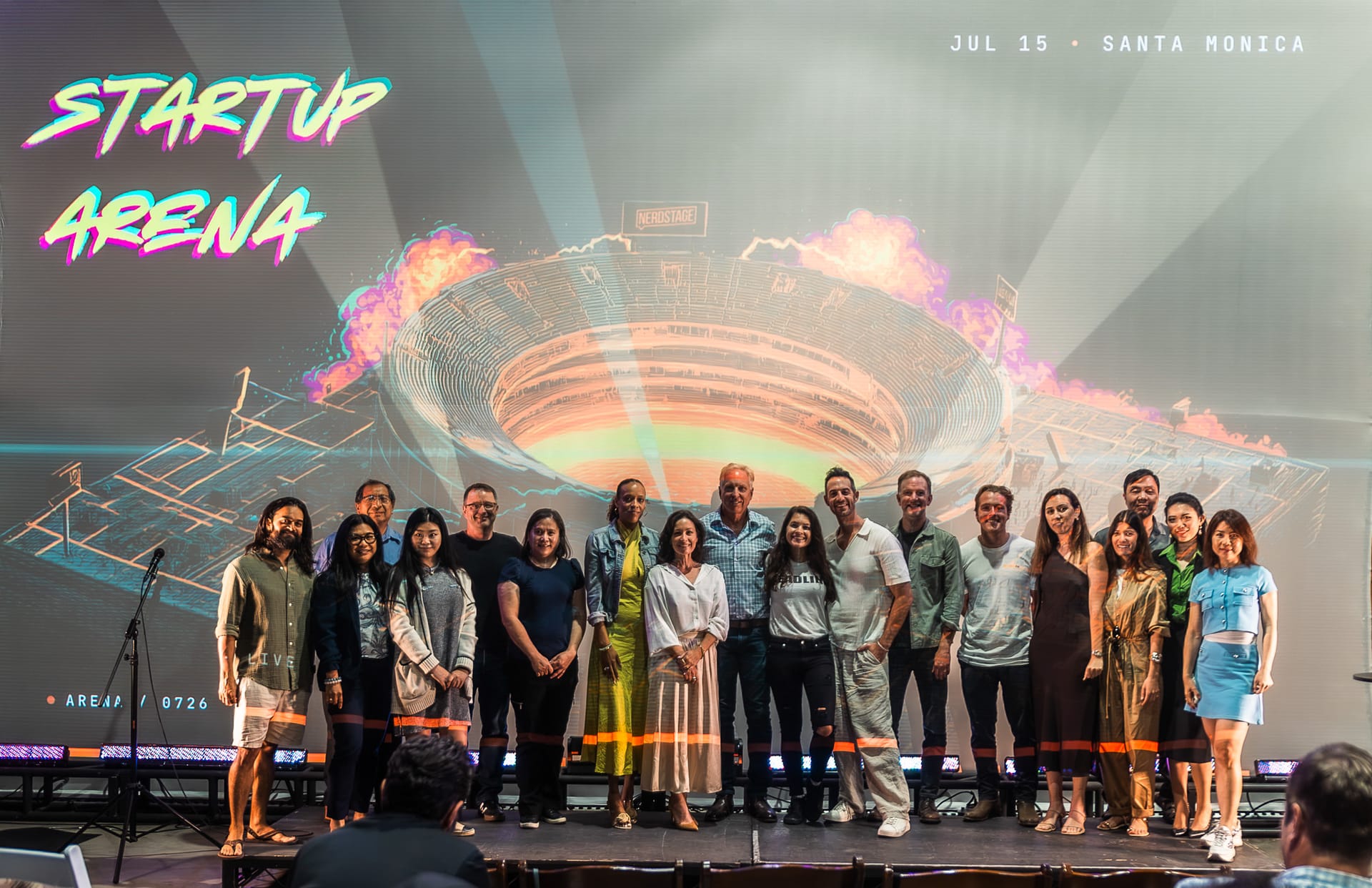 Founders and investors lined up on stage for a group photo in front of the projected Startup Arena stadium backdrop reading Jul 15 · Santa Monica