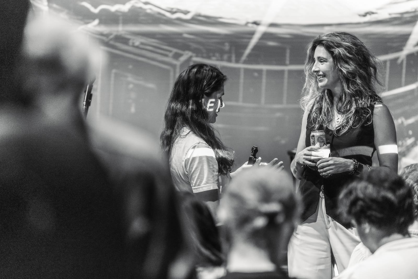 Two attendees talking and smiling over drinks during the networking hour, the event projection glowing behind them