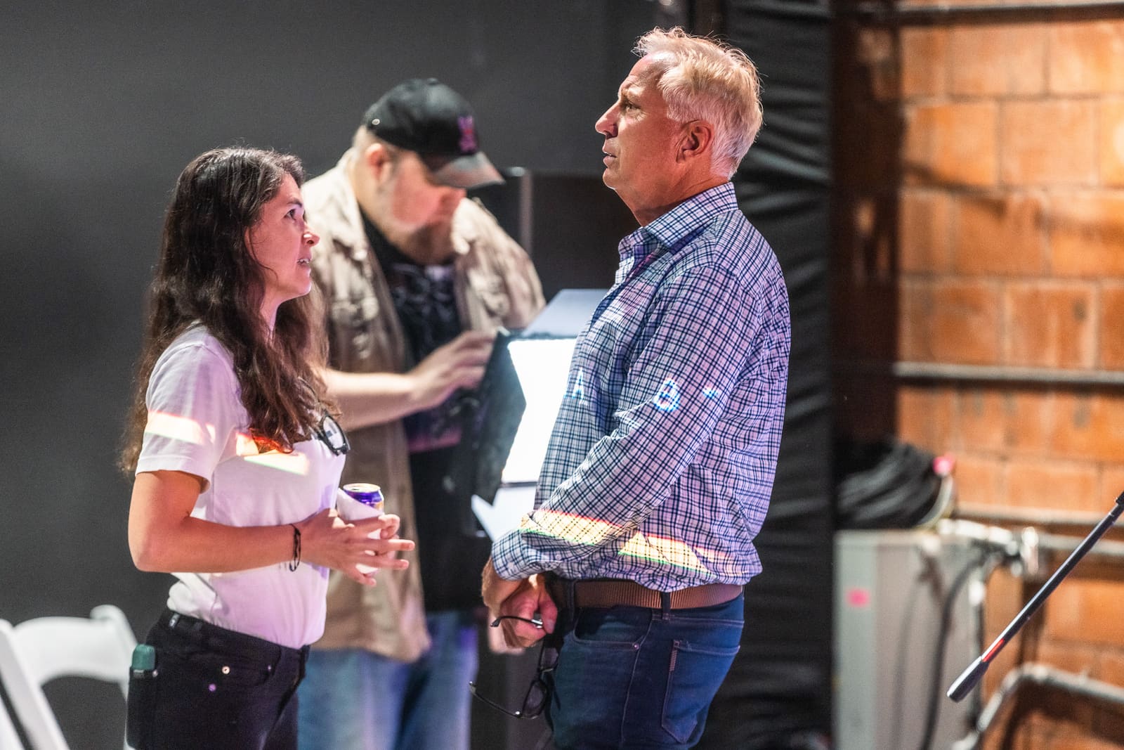 Two attendees in conversation near the stage, one mid-sentence with a drink in hand, the other listening