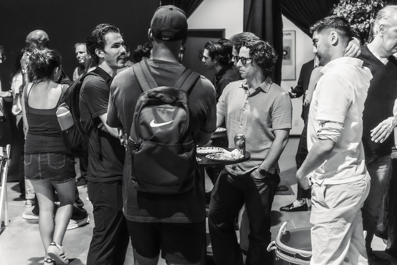 Black and white: a circle of attendees talking around a high table with plates and drinks