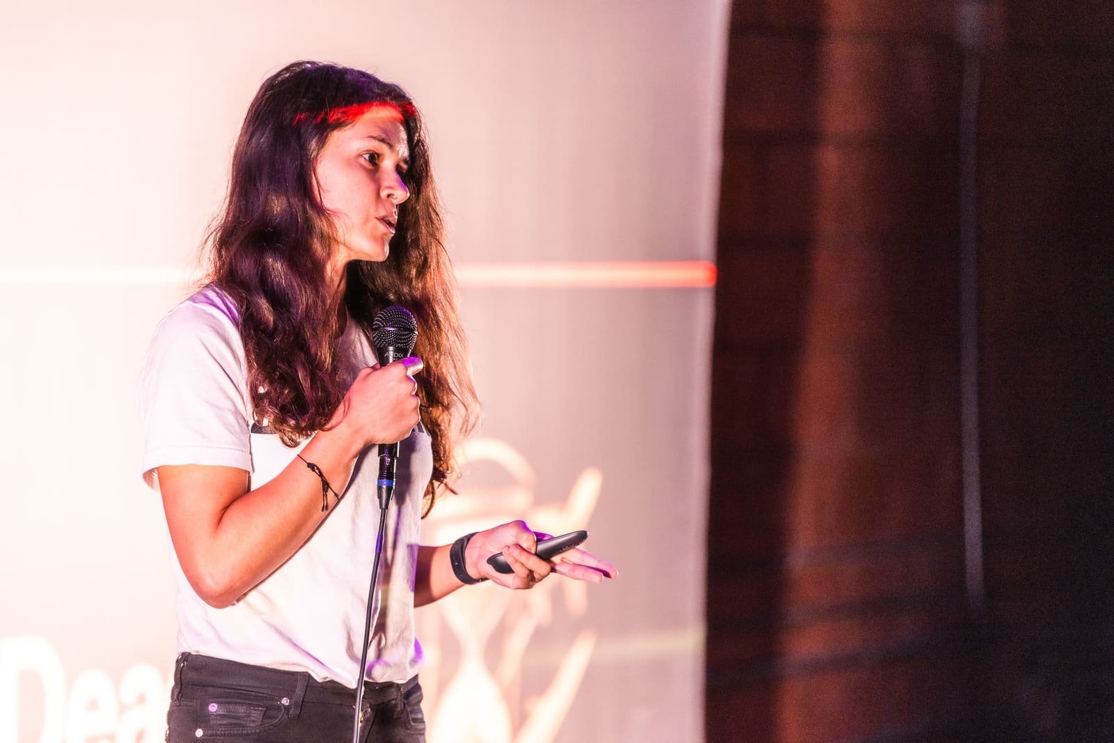 Elvina Beck of Deadline pitching with mic and clicker under warm rim light, the Deadline logo projected behind her