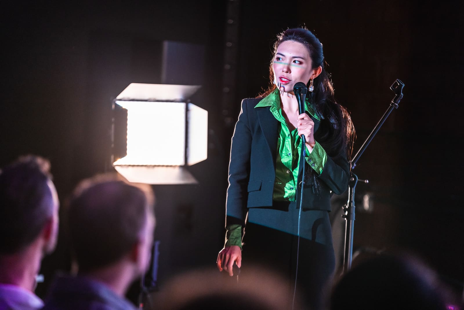 Linran Yu of LA Preferred pitching in a green satin shirt, mic in hand, stage light glowing at left