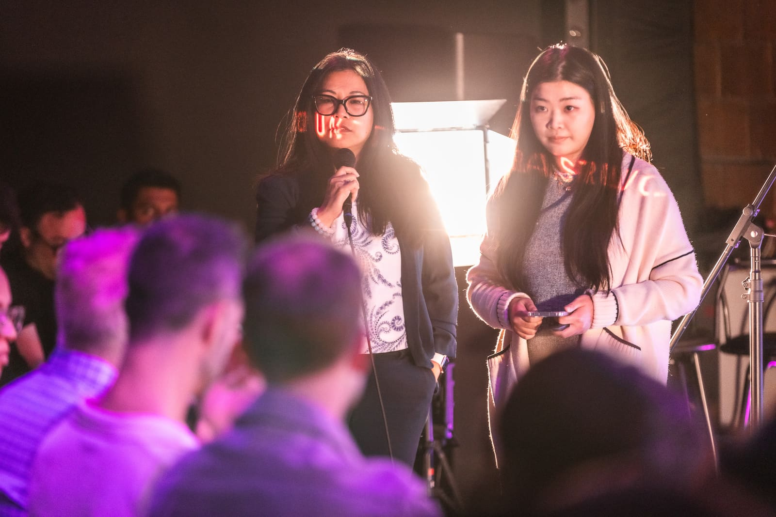 Nancy Tang of Numeris Ledger speaking into a mic beside her co-presenter, backlit by a stage softbox