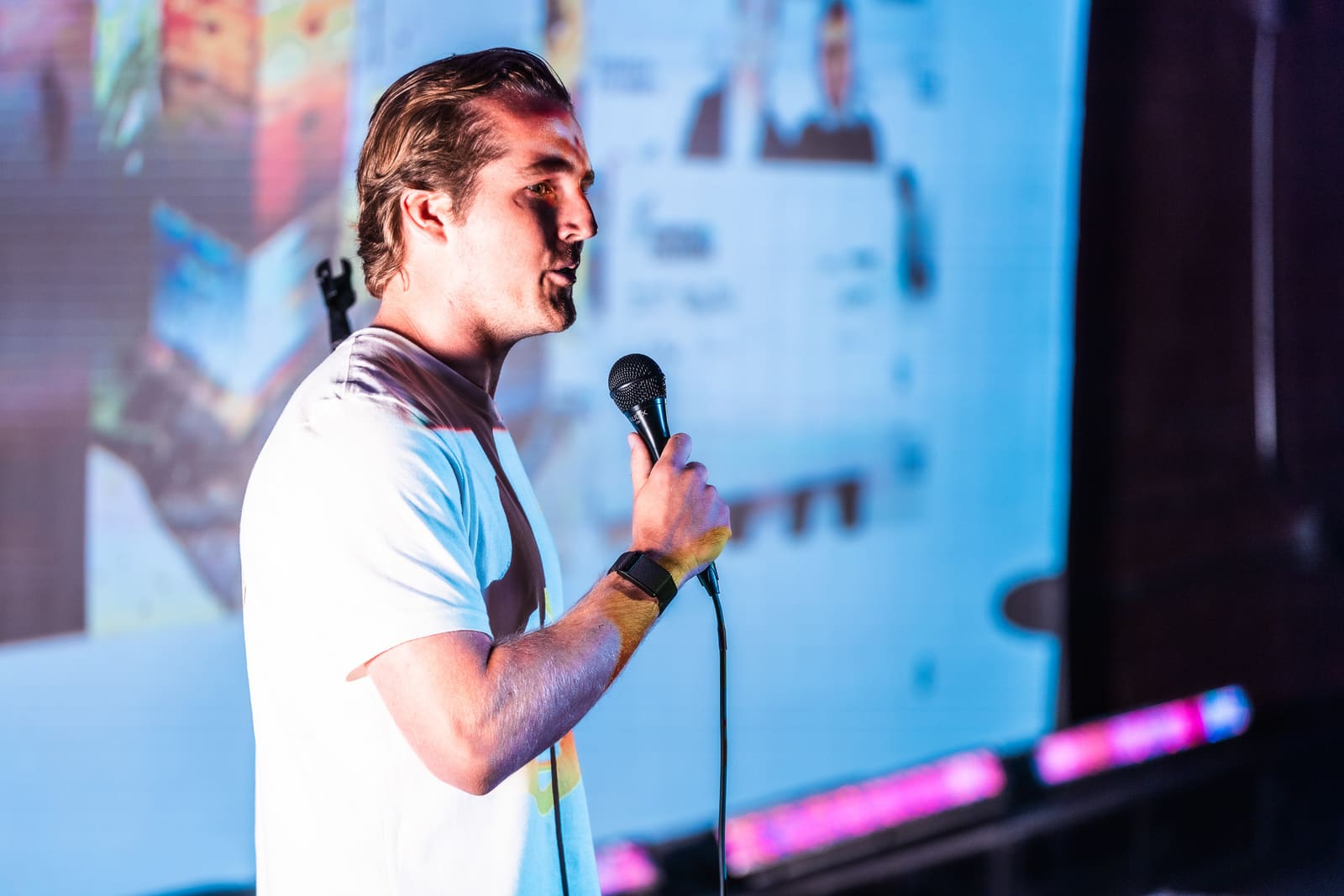 Robert Schulte of PollenPal in profile pitching with a mic in front of a blue projected product collage