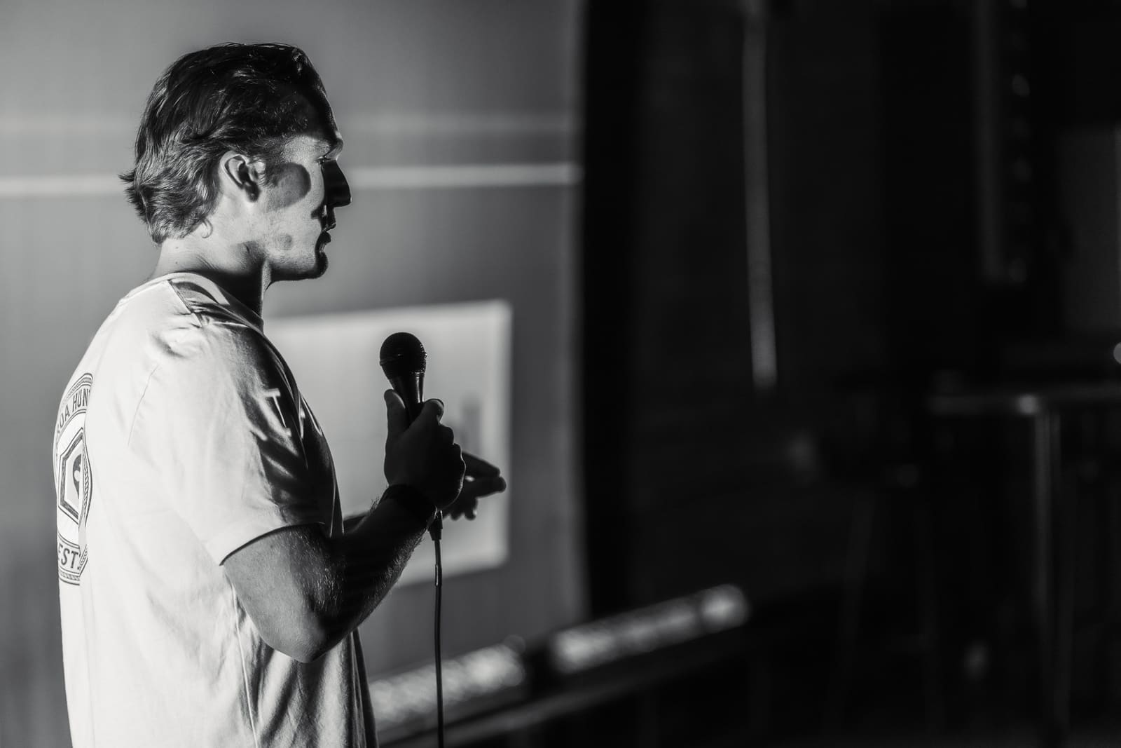 Robert Schulte of PollenPal in profile holding a mic on a dark stage, his face half-lit by projection light