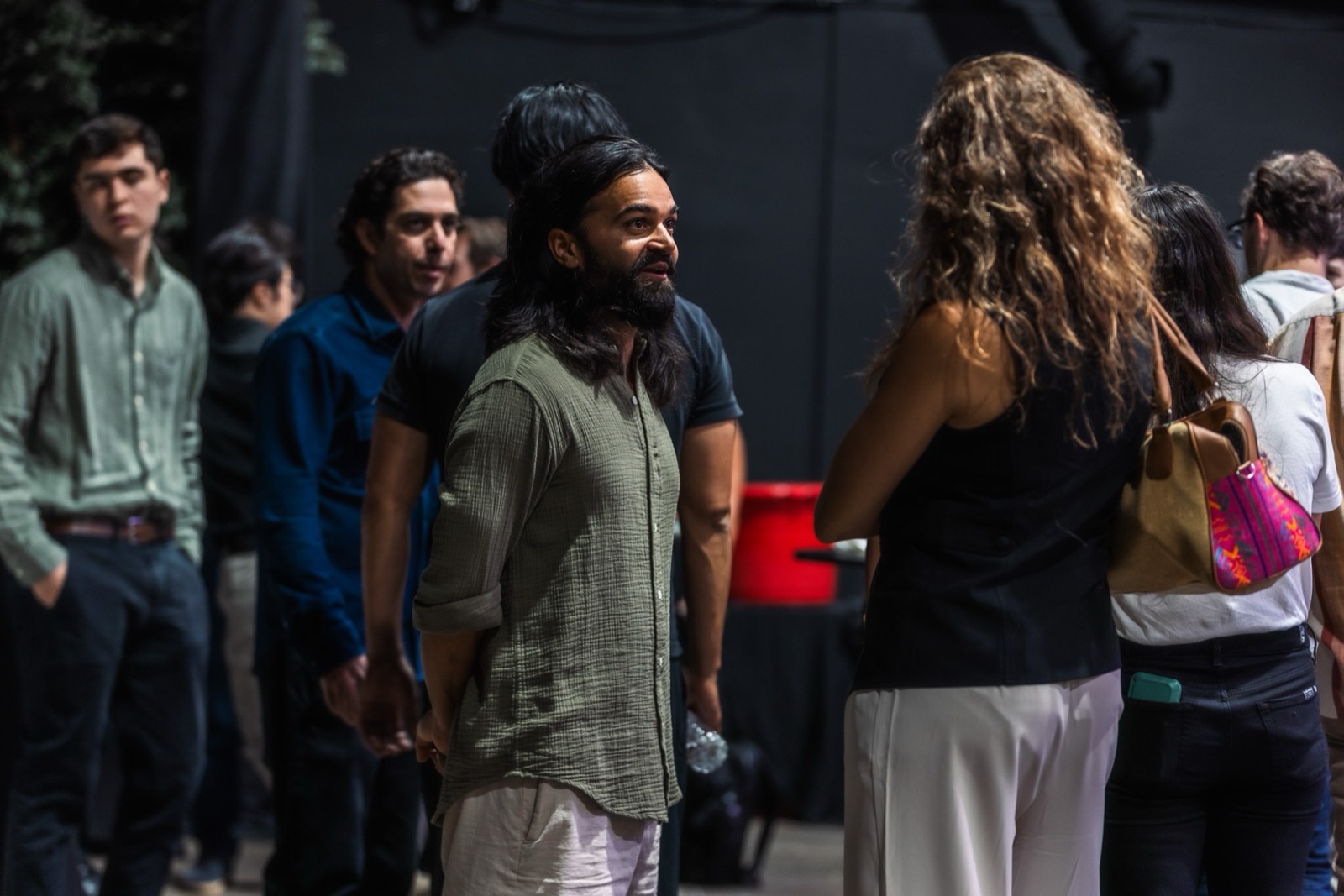 A founder with long hair and a beard mid-conversation in a crowd, people talking in small groups behind him
